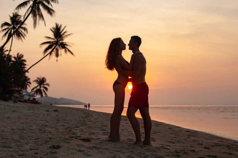 young sexu romantic couple in love on sunset happy on summer beach together having fun wearing swim suits